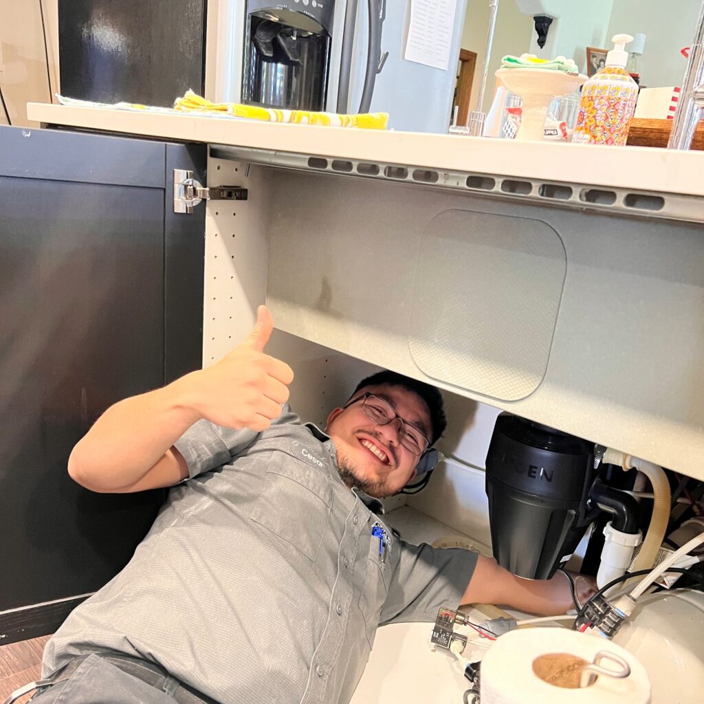 Amped plumber repairing garbage disposal under sink in Oklahoma.