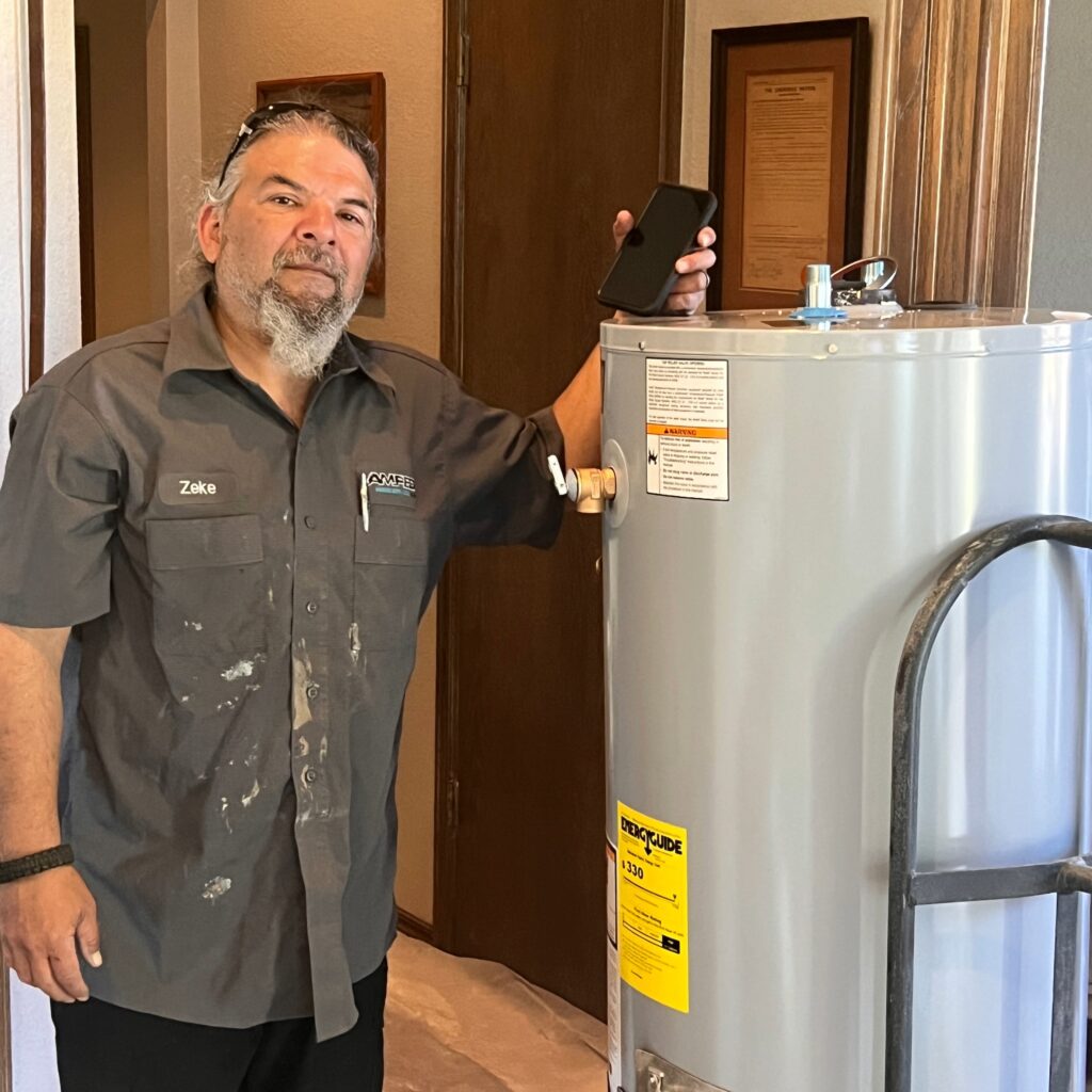 Amped plumber standing beside residential water heater in Oklahoma.