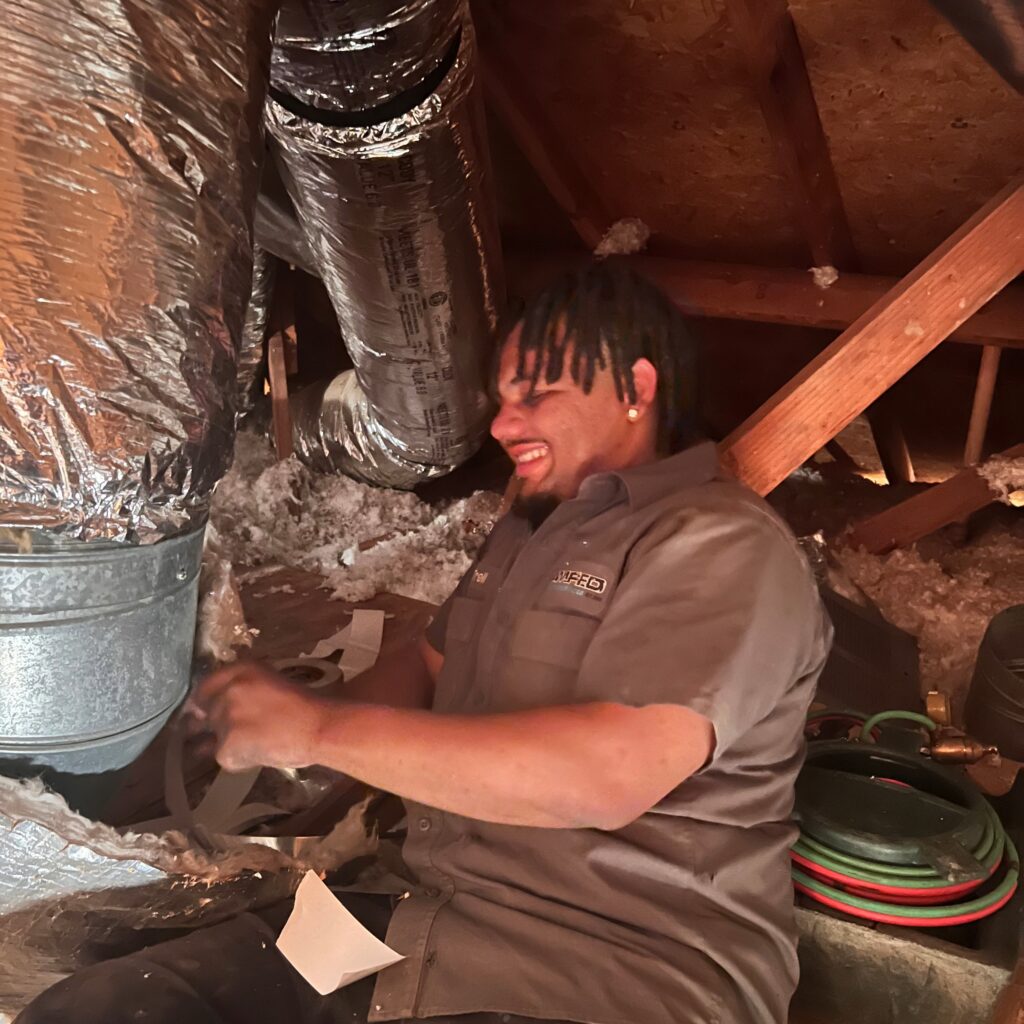 Amped HVAC technician repairing ductwork in Oklahoma attic.