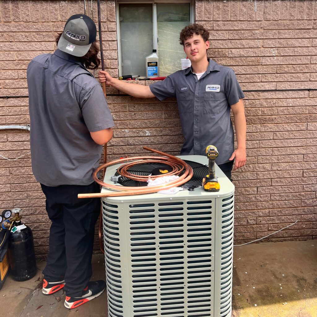 Amped HVAC technicians servicing outdoor air conditioning unit in Oklahoma.