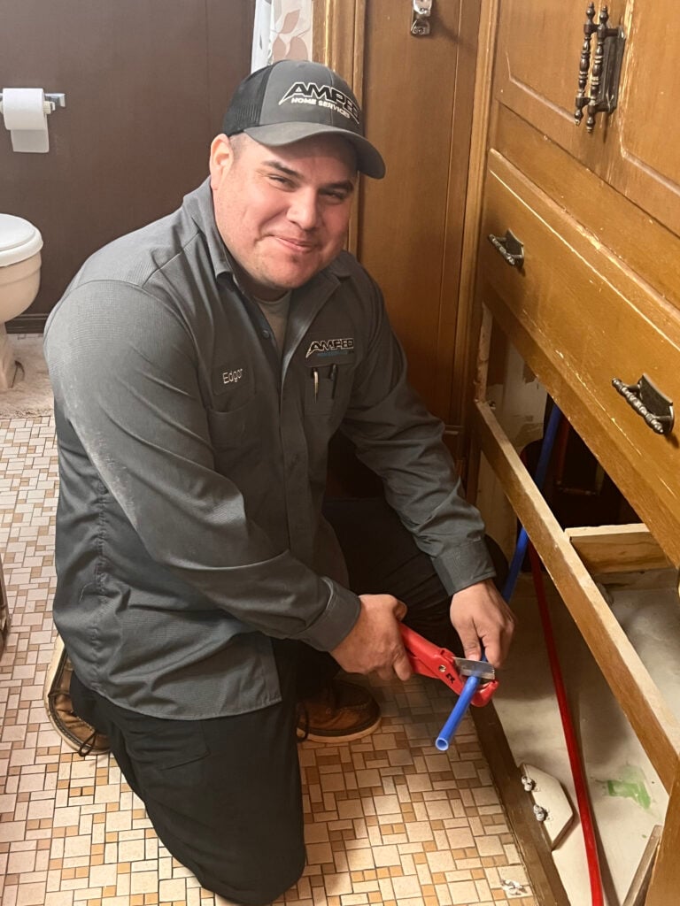 Amped plumber repairing pipes under a sink in Oklahoma.