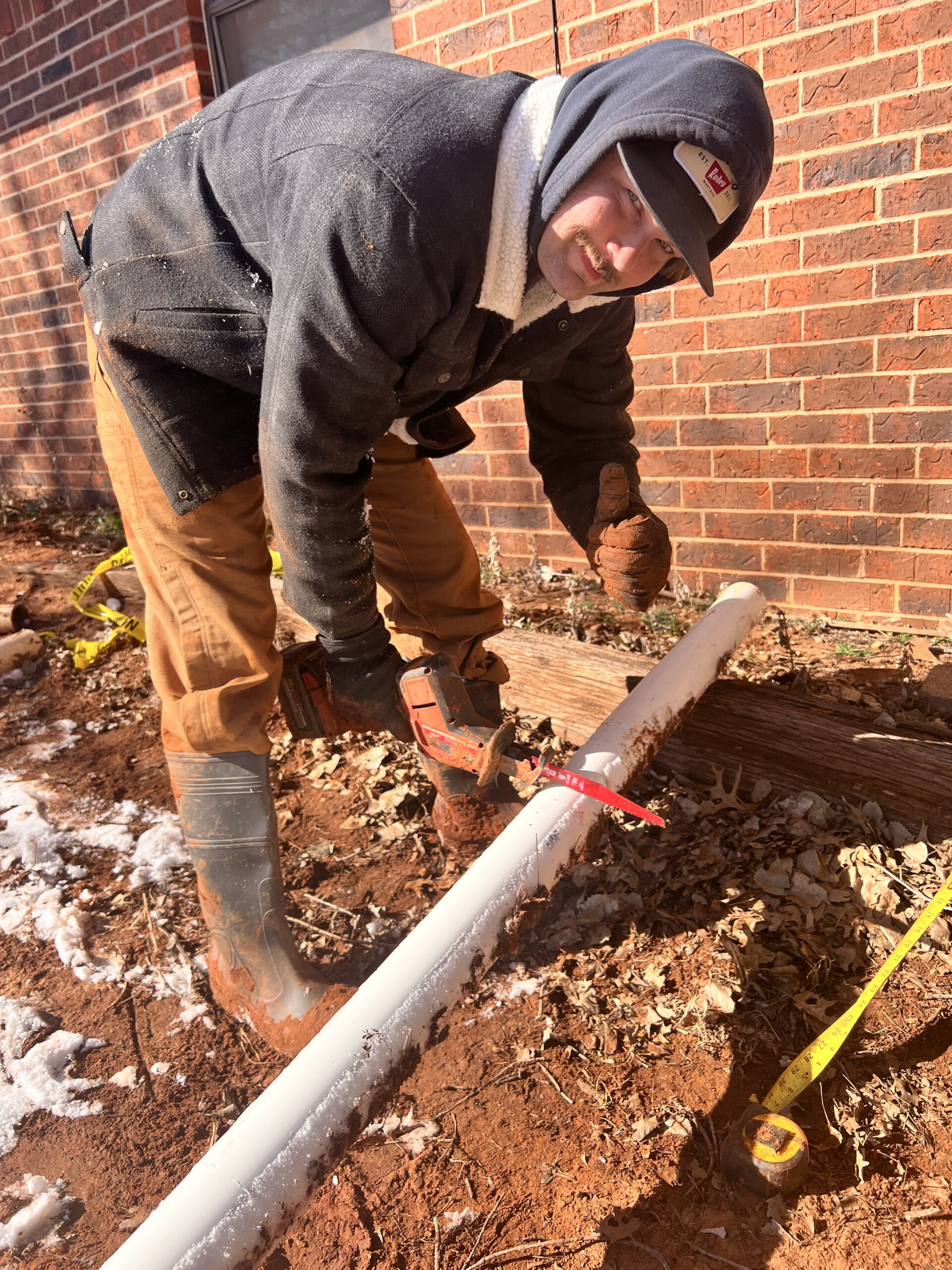 Amped technician cutting PVC pipe during underground plumbing repair in Oklahoma.