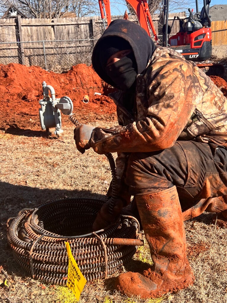 Amped plumber operating a drain snake for sewer cleaning in Oklahoma.
