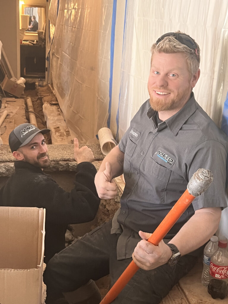 Amped plumbers using pipe wrench during plumbing repair in Oklahoma.