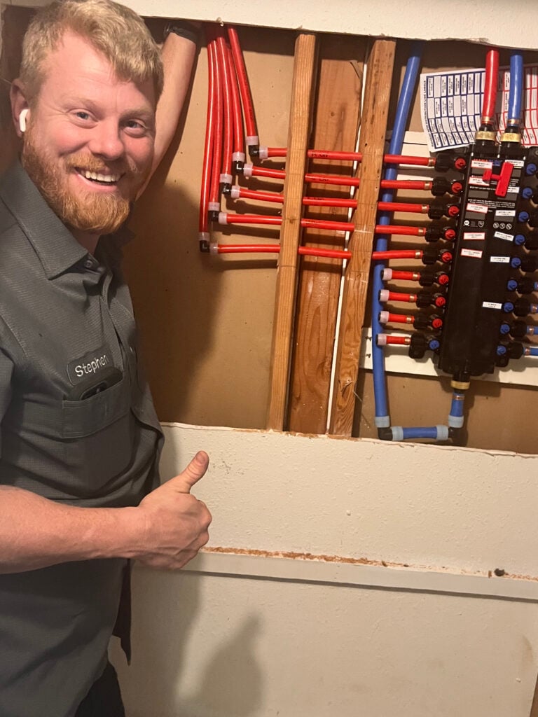 Amped plumber inspecting residential plumbing manifold in Oklahoma.