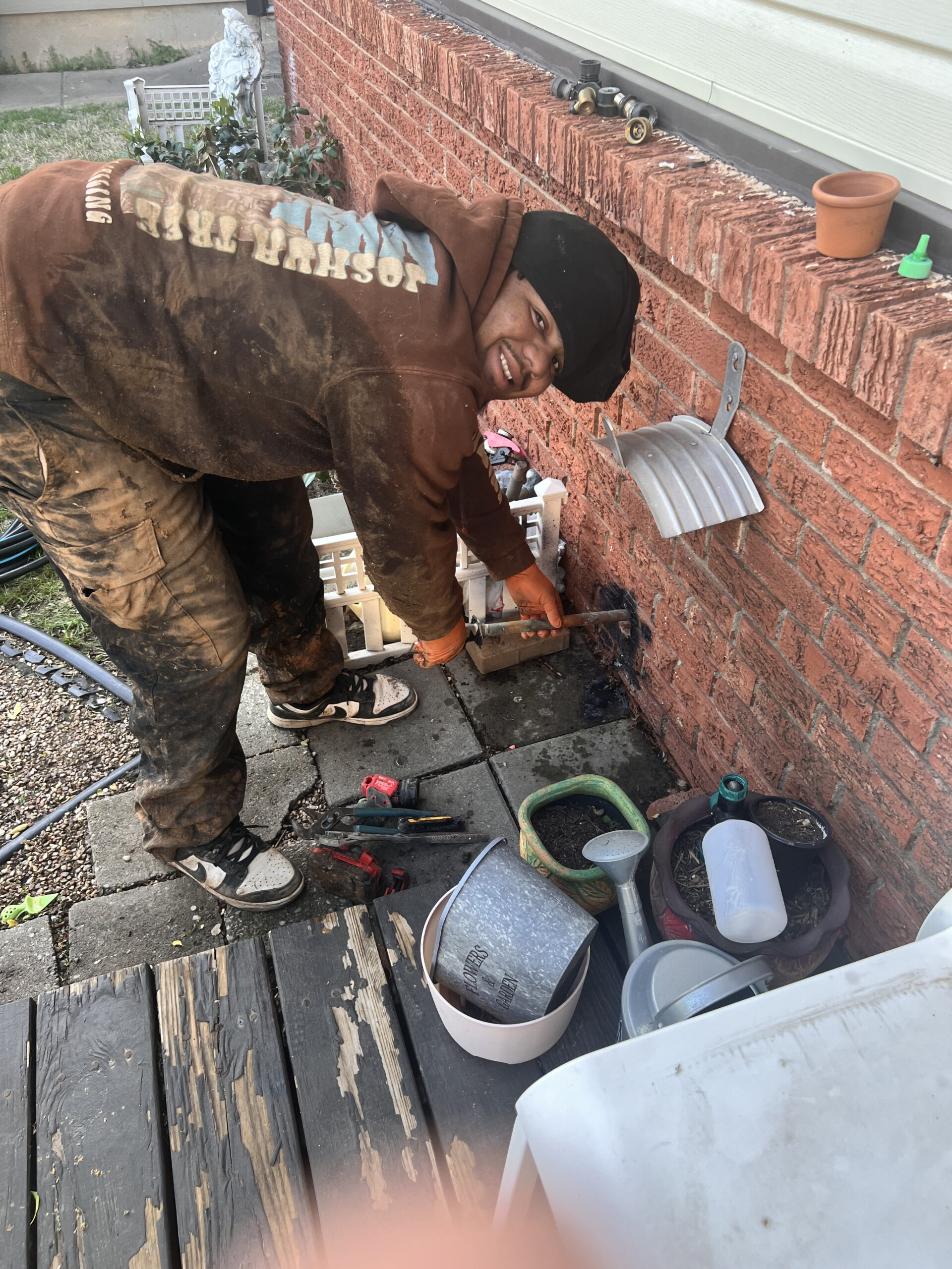 Amped plumber repairing water line along brick wall in Oklahoma.