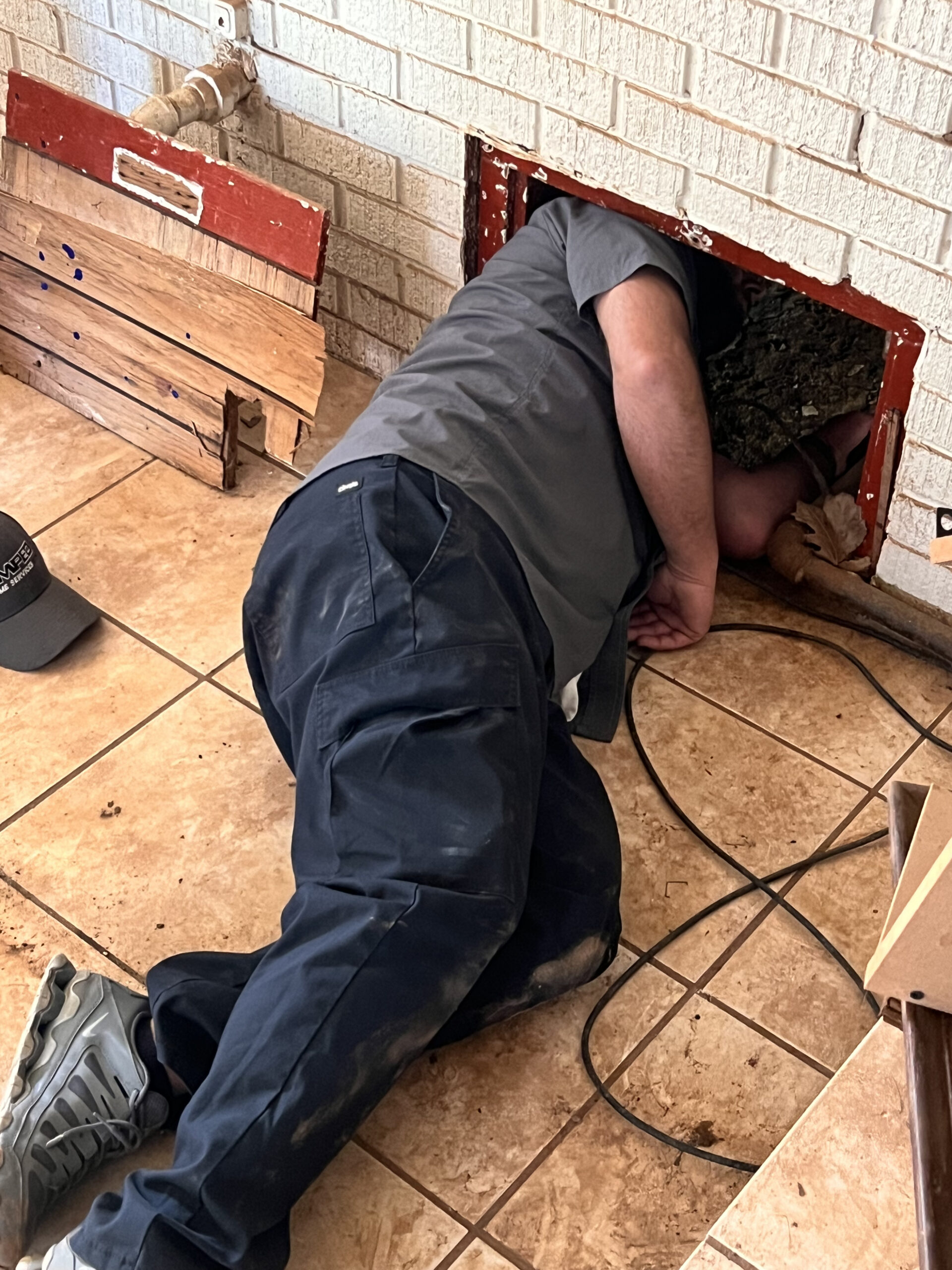 Amped plumber accessing plumbing through floor panel in Oklahoma.