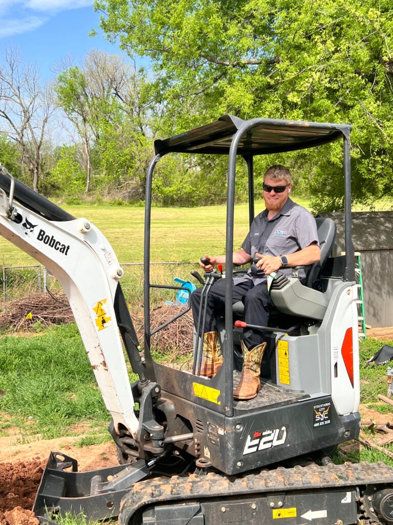 Amped technician using mini excavator for plumbing excavation in Oklahoma.