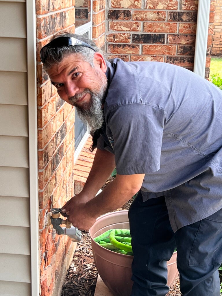 Amped plumber repairing outdoor faucet in Oklahoma.