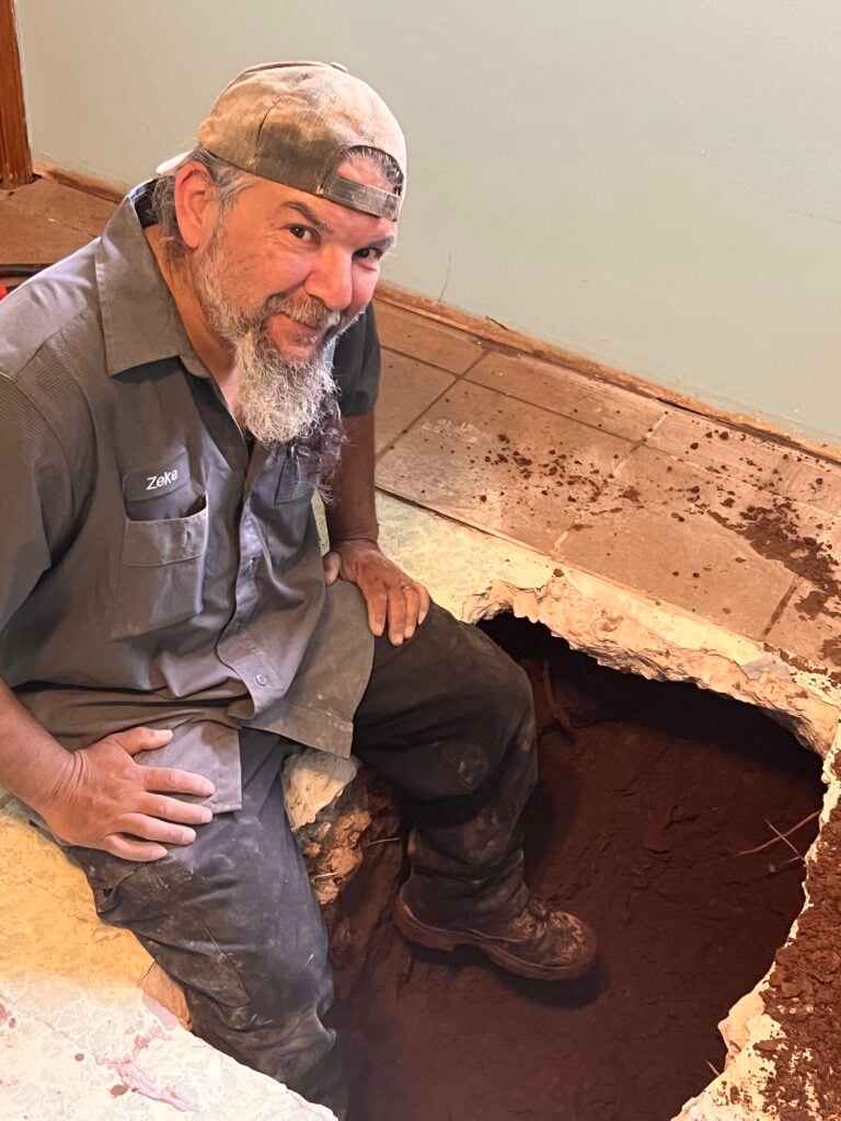 Amped plumber repairing underground plumbing through floor cutout in Oklahoma.