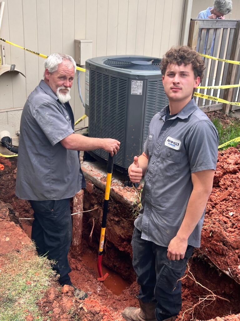 Amped plumbers repairing underground plumbing near HVAC unit in Oklahoma.