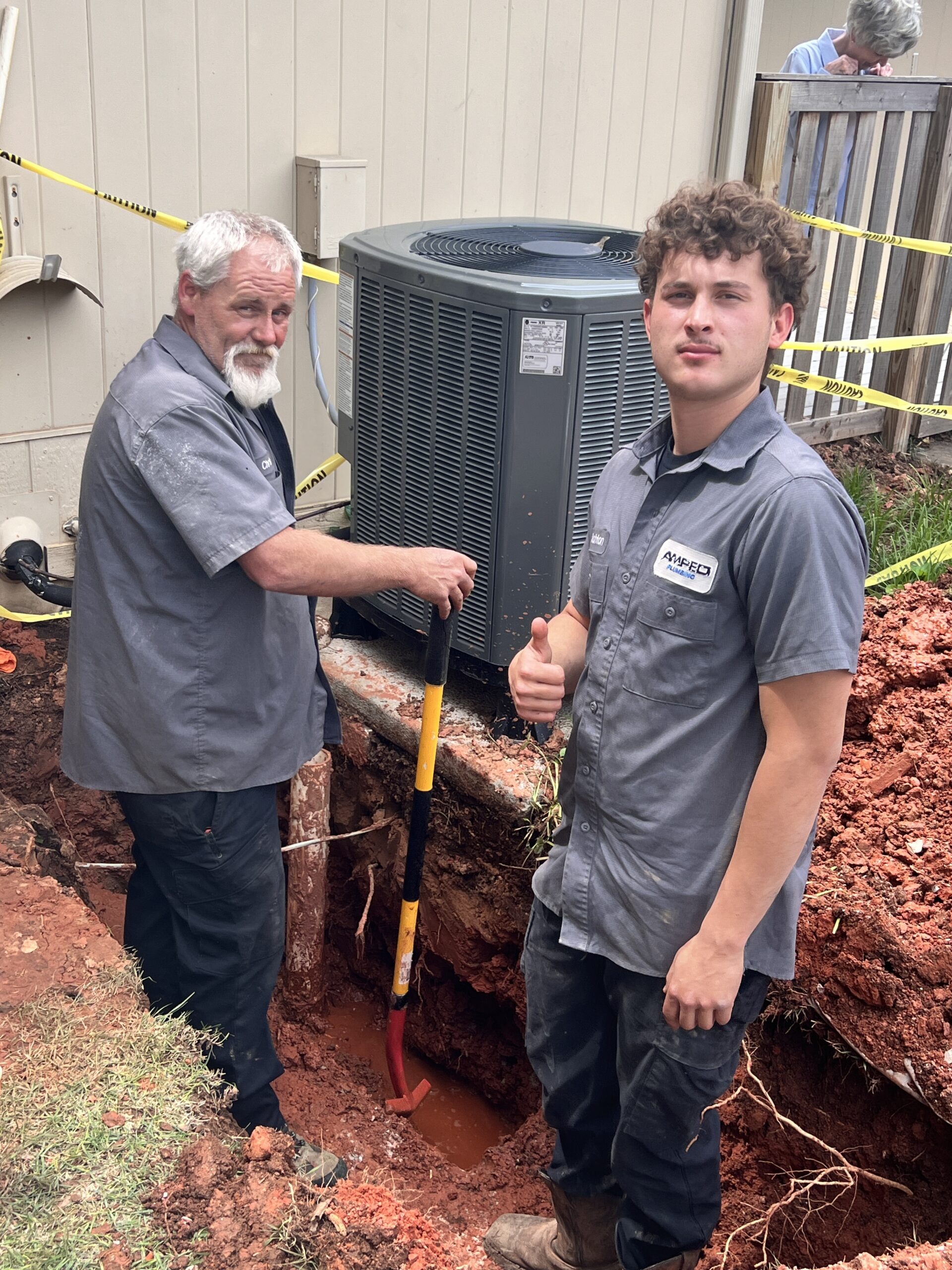 Amped plumbers repairing underground plumbing near HVAC unit in Oklahoma.