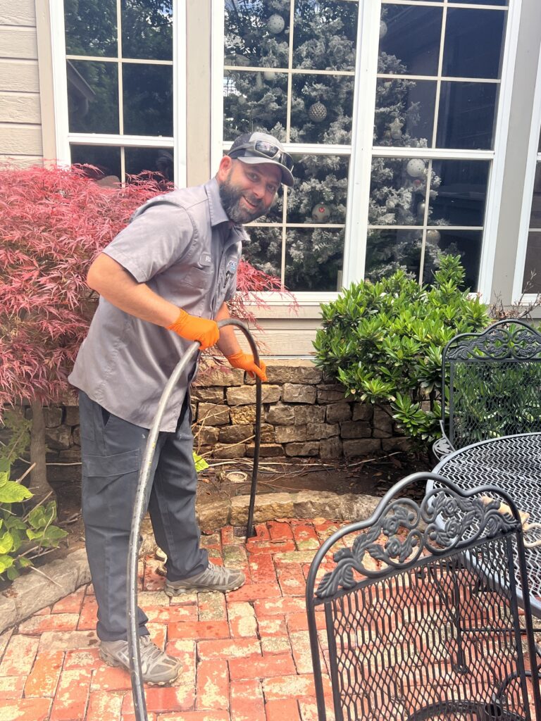 Amped plumber operating drain snake on outdoor patio in Oklahoma.