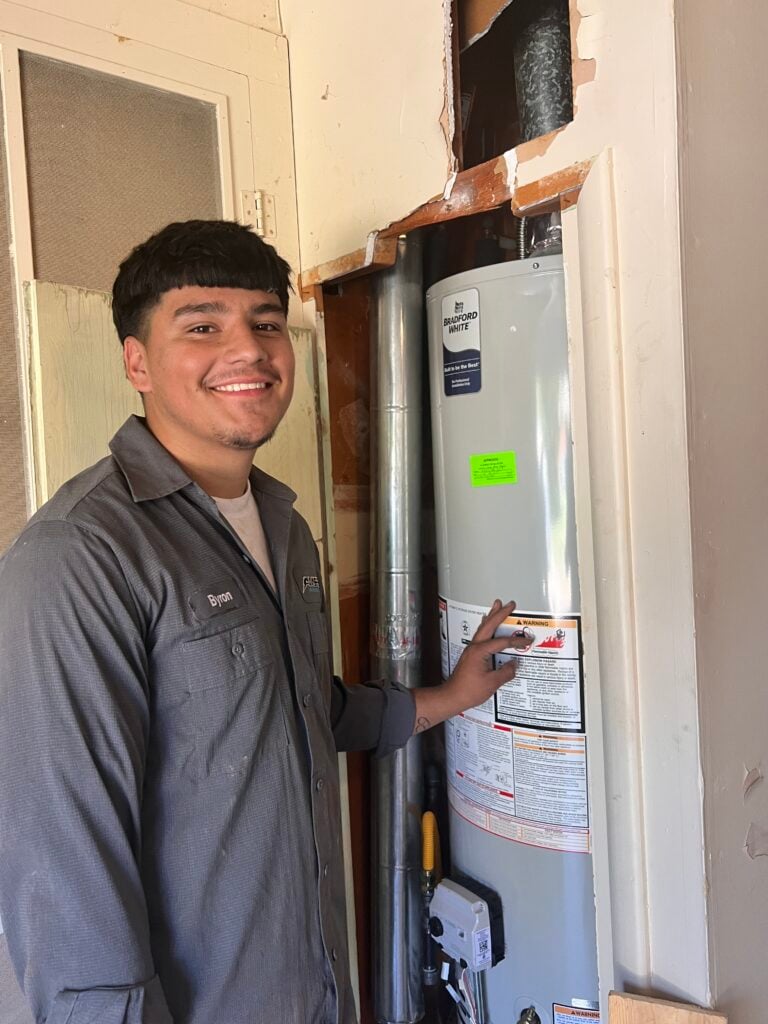 Amped plumber inspecting residential water heater in Oklahoma.