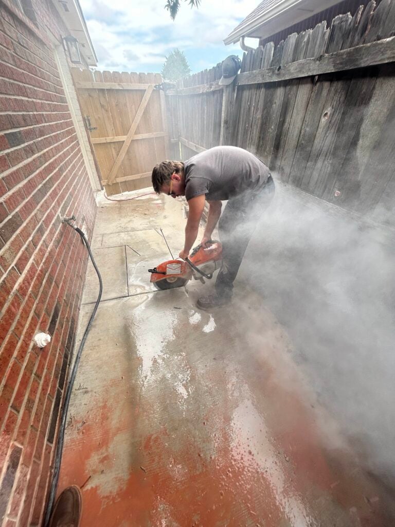 Amped plumber cutting concrete slab for plumbing access in Oklahoma.