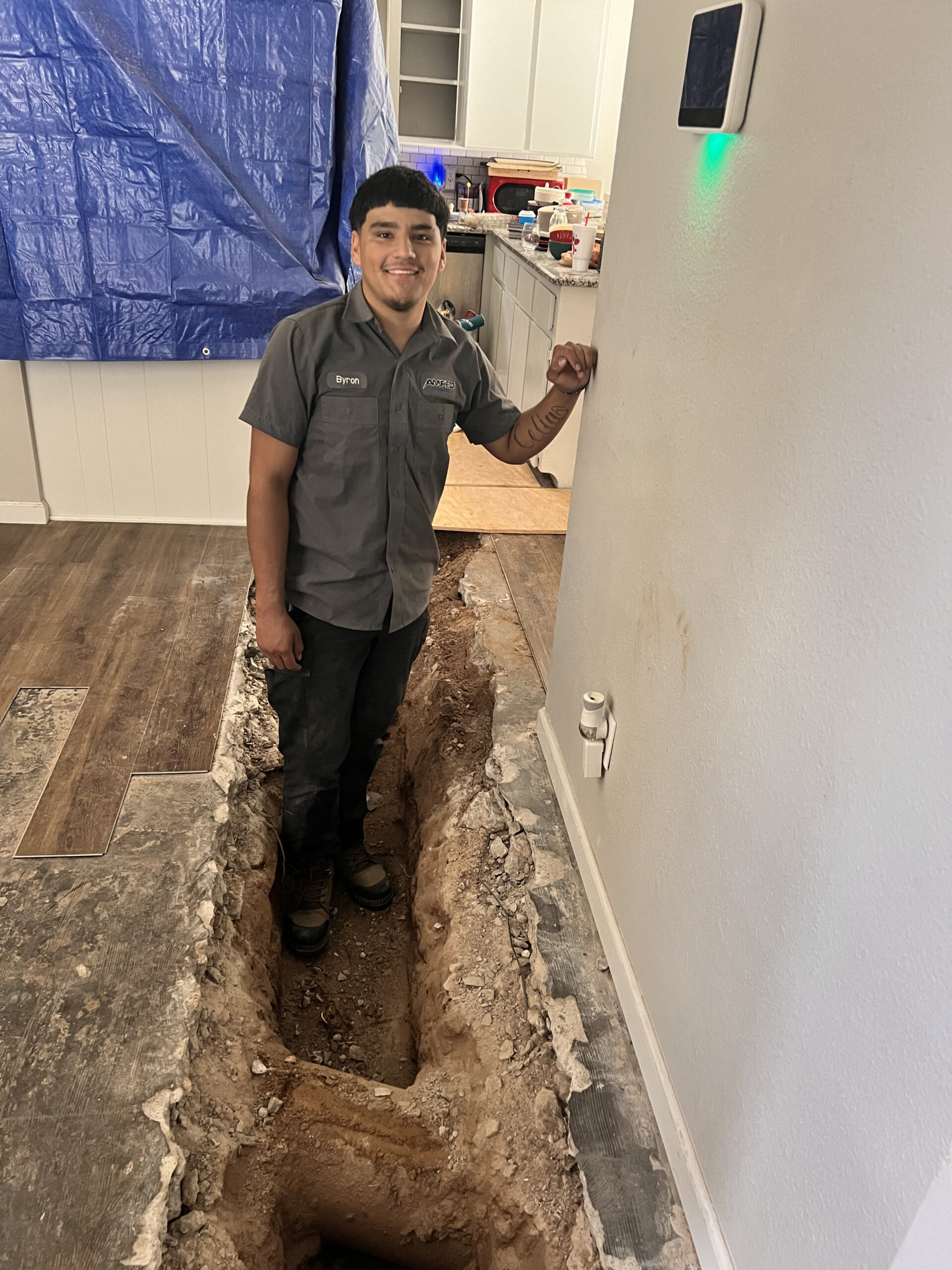 Amped plumber standing in indoor trench during plumbing repair in Oklahoma.