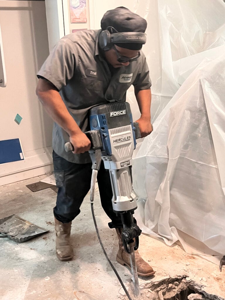 Amped plumber using jackhammer to access plumbing under concrete floor in Oklahoma.