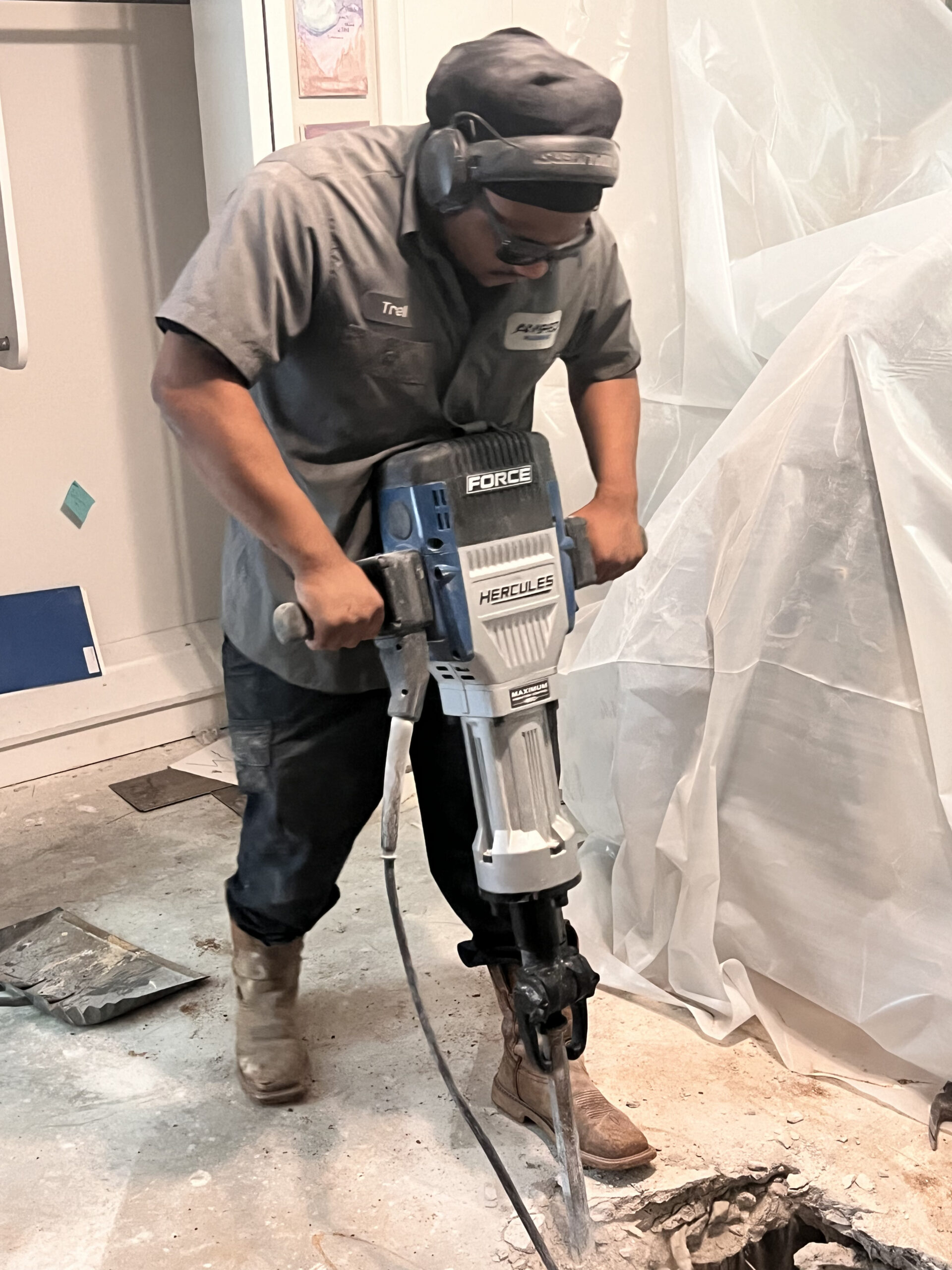Amped plumber using jackhammer to access plumbing under concrete floor in Oklahoma.