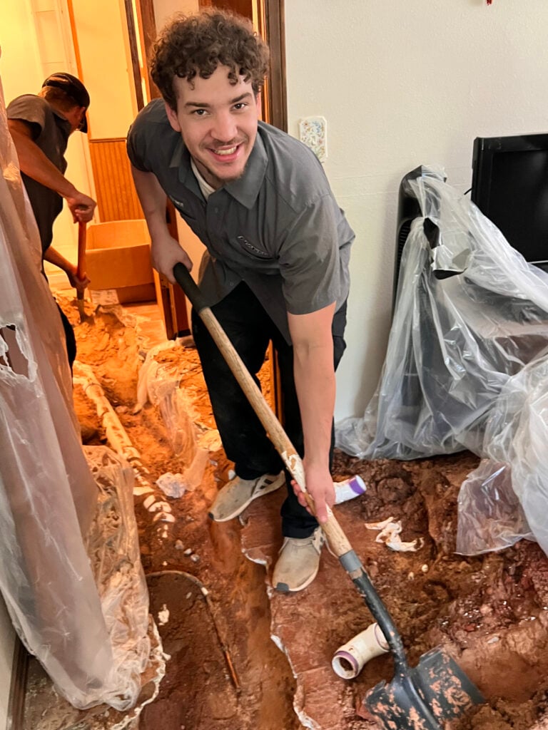 Amped plumber repairing pipes through indoor trench in Oklahoma.