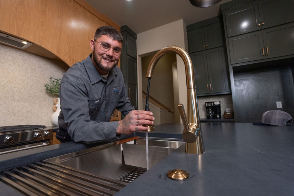 Amped technician smiling by a kitchen sink faucet.