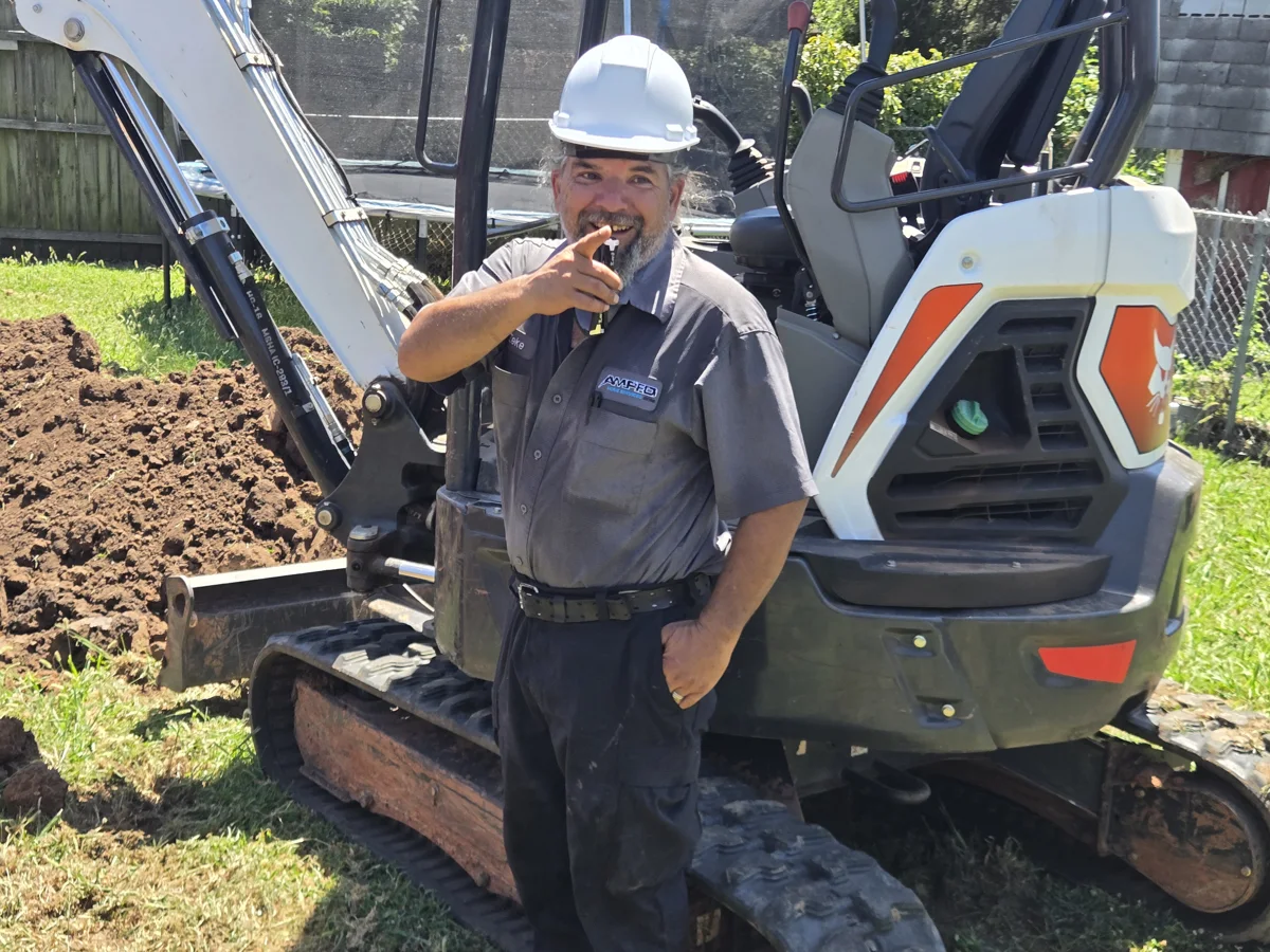 Amped technician wearing a hard hat beside an excavator