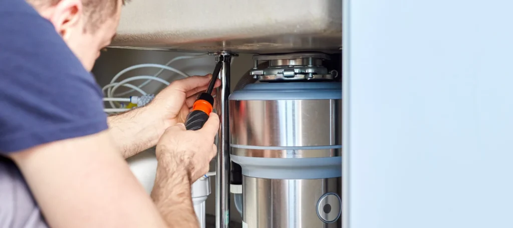 Technician servicing a garbage disposal beneath a kitchen sink