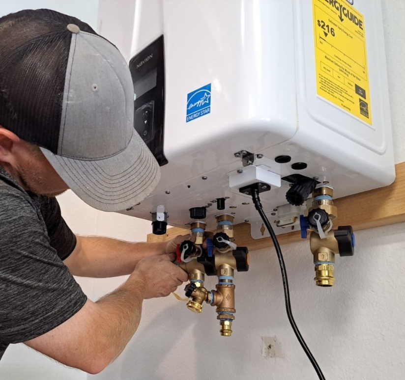 Technician servicing valves beneath a wall-mounted tankless water heater