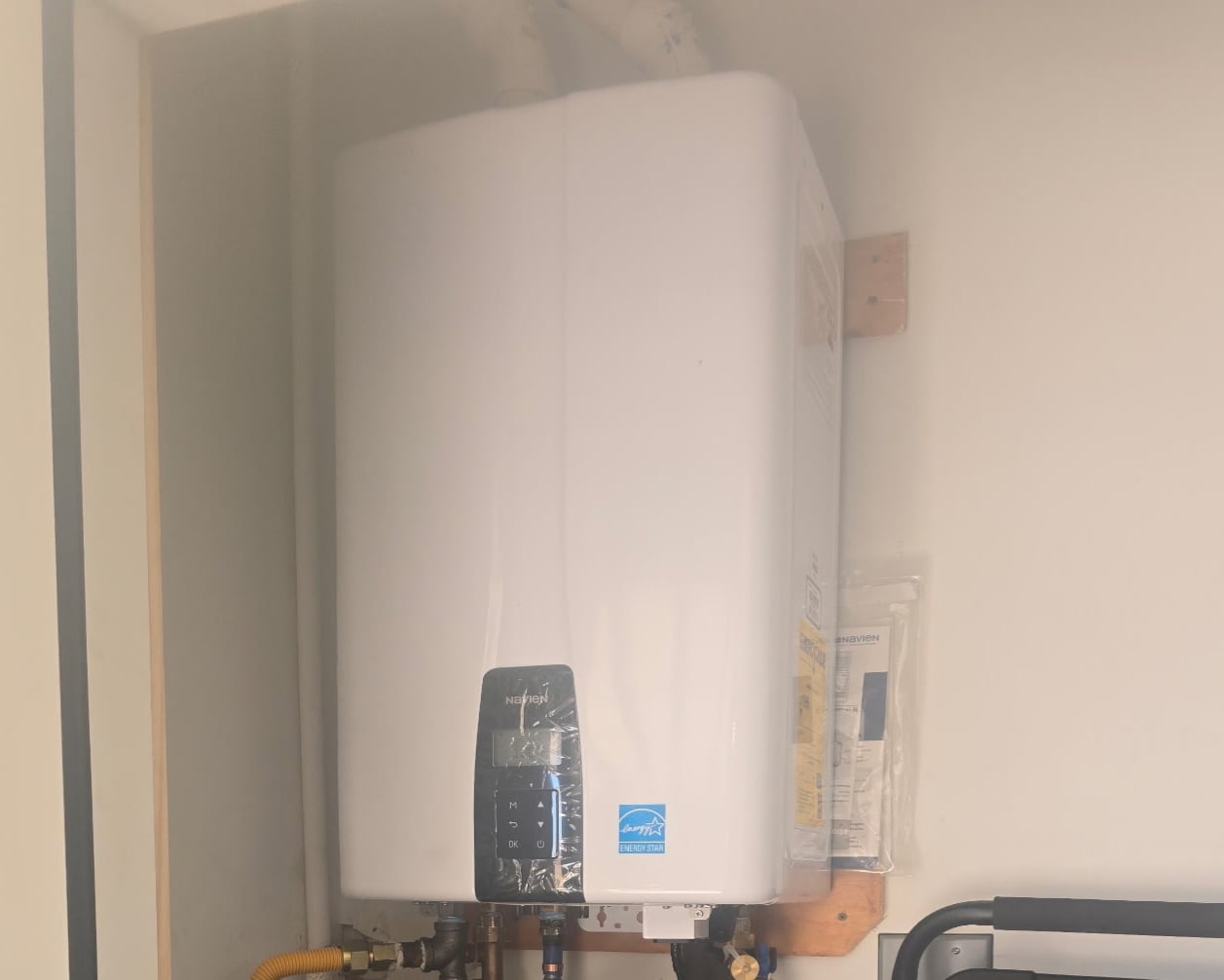 Wall-mounted Navien tankless water heater with digital controls and plumbing connections below.