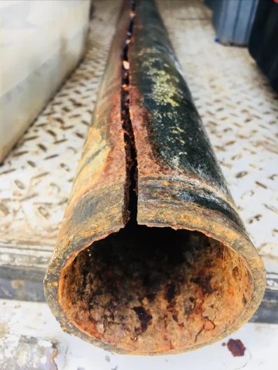 Removed cast-iron sewer pipe with a long split and heavy corrosion visible inside