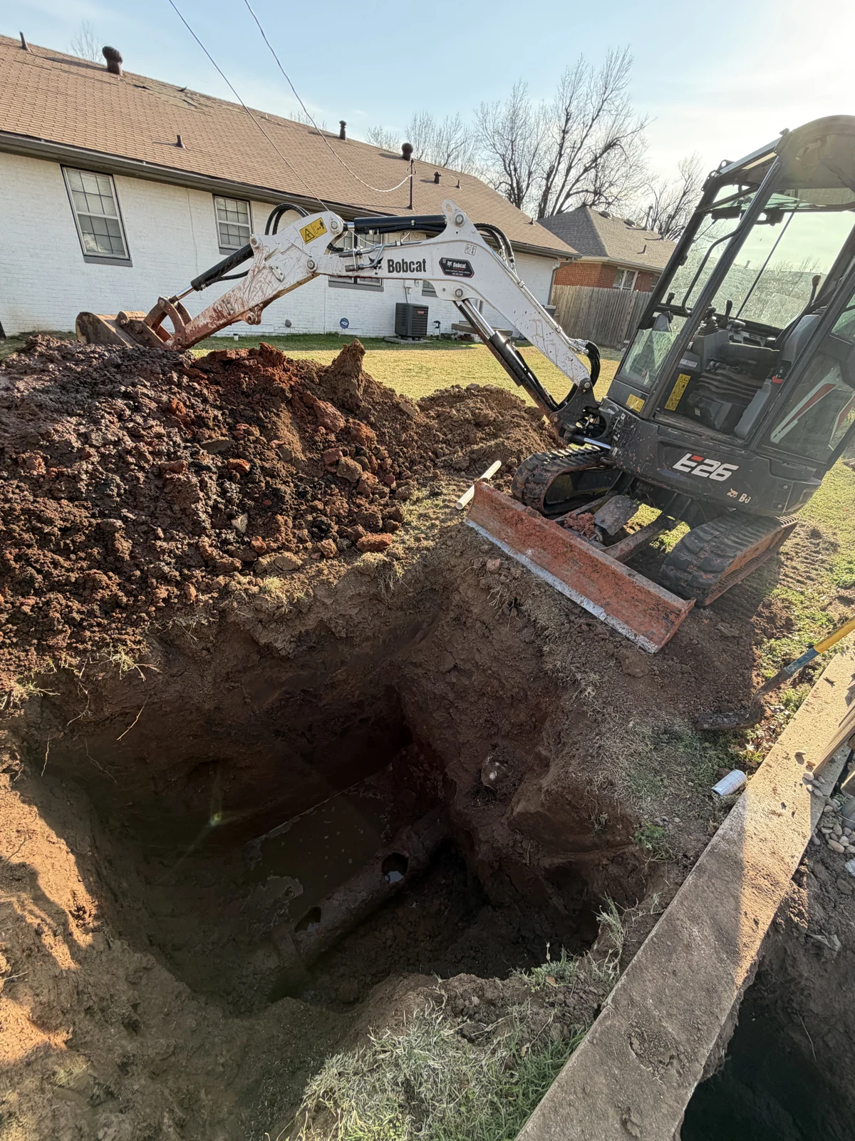 Excavator beside an open sewer-line trench at an Amped job