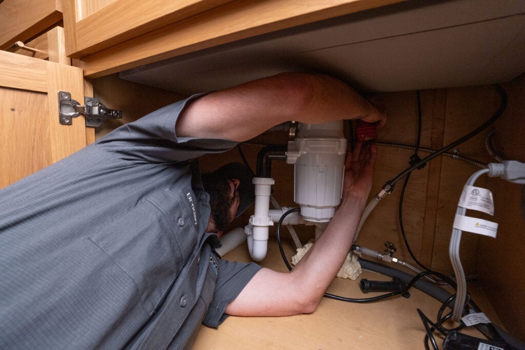 Plumber inspecting and repairing under-sink drain plumbing.