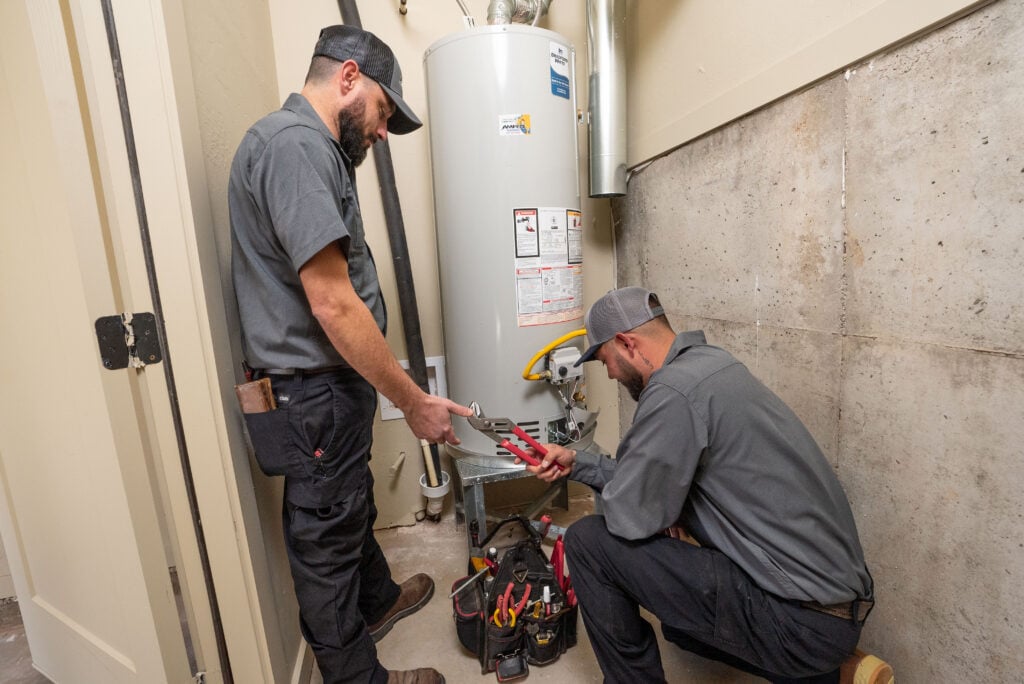 Two plumbers inspecting and servicing a residential tank water heater.