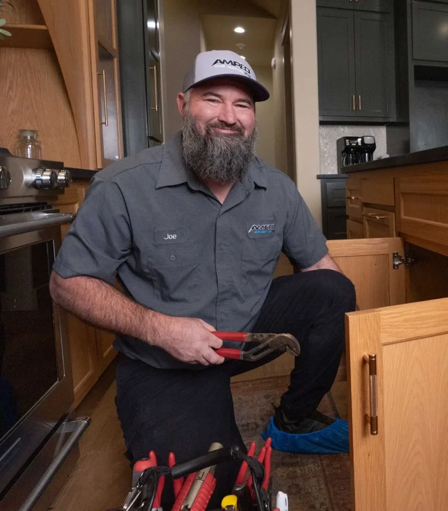 Amped plumber in uniform holding pliers beside an open kitchen sink cabinet